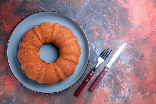 Vista superior tenedor y cuchillo de pastel junto al apetitoso pastel en el plato