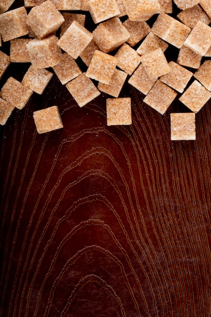 Foto gratuita vista superior de terrones de azúcar morena esparcidos sobre fondo de madera con espacio de copia