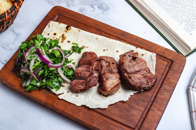 Vista superior tika kebab en pan de pita con hierbas y cebollas en una pizarra