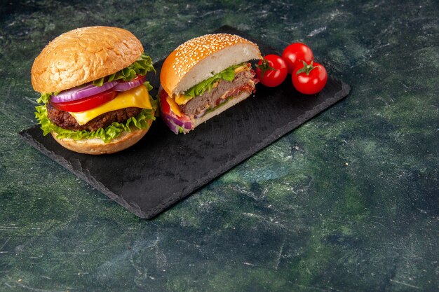 Vista superior de todo corte varios sabrosos sándwiches y tomates con tallo en bandeja negra en la parte superior en la superficie de color oscuro de mezcla
