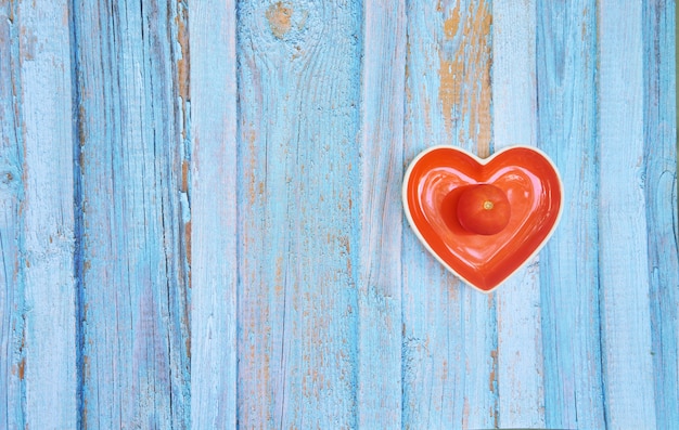 Vista superior de tomate en un recipiente con forma de corazón sobre la superficie de madera azul