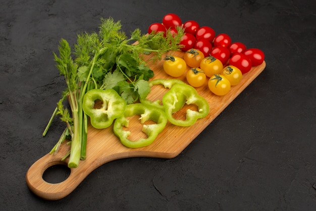 vista superior tomates amarillos y rojos junto con pimiento verde en rodajas y hojas verdes en el piso oscuro