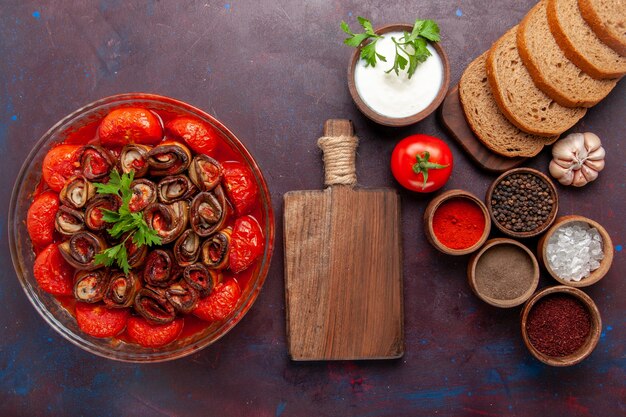 Vista superior de tomates y berenjenas de comida vegetal cocida con condimentos y panes de pan en el escritorio oscuro
