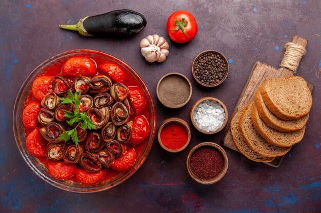 Vista superior de tomates y berenjenas de comida vegetal cocida con pan de condimentos en una superficie oscura