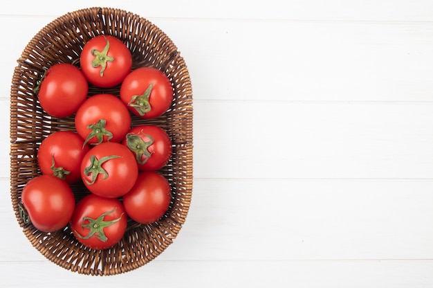 Vista superior de tomates en la canasta en el lado izquierdo y superficie blanca con espacio de copia