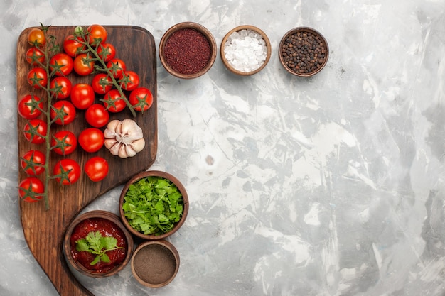Vista superior de tomates cherry frescos con condimentos y verduras sobre superficie blanca