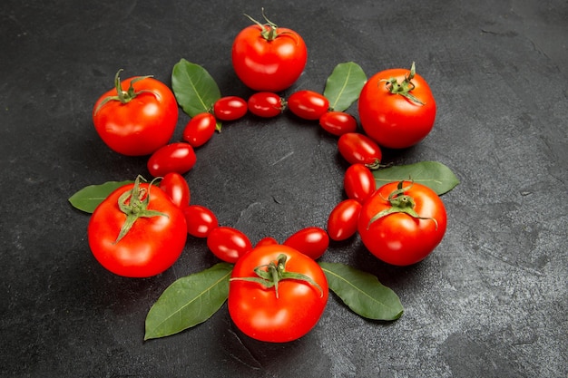 Vista superior de tomates cherry y hojas de laurel rojo sobre suelo oscuro con espacio libre