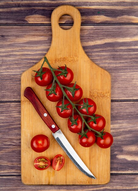 Vista superior de tomates cortados y enteros con cuchillo en la tabla de cortar en madera