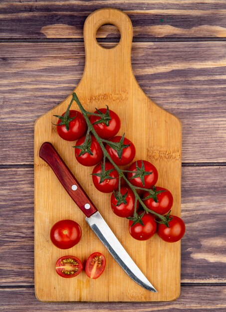 Vista superior de tomates cortados y enteros con cuchillo en la tabla de cortar sobre superficie de madera