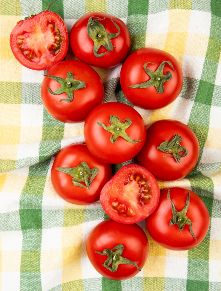 Foto gratuito vista superior de tomates cortados y enteros sobre una superficie de tela escocesa