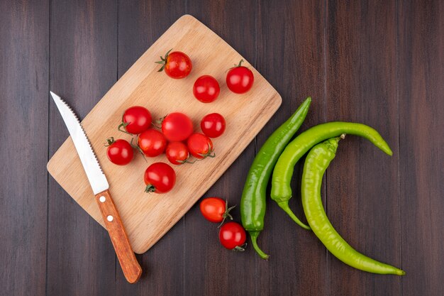 Vista superior de tomates y cuchillo en la tabla de cortar con pimientos sobre superficie de madera