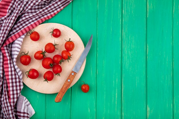 Vista superior de tomates y cuchillo en tabla de cortar con tela escocesa sobre superficie verde