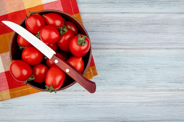 Vista superior de tomates con cuchillo en un tazón sobre tela y superficie de madera con espacio de copia
