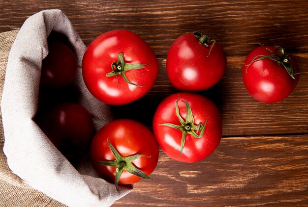 Vista superior de tomates derramando saco sobre superficie de madera