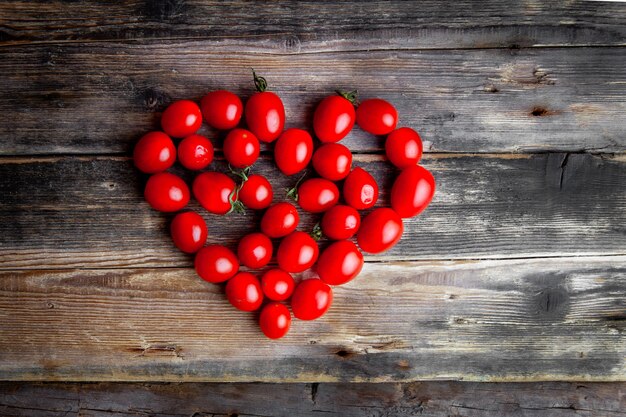 Vista superior de tomates formando forma de corazón sobre fondo de madera oscura. espacio horizontal para texto