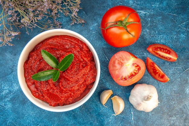 Vista superior de tomates frescos con pasta de tomate y ajo en mesa azul