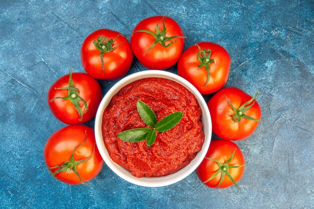 Vista superior de tomates frescos con pasta de tomate en mesa azul