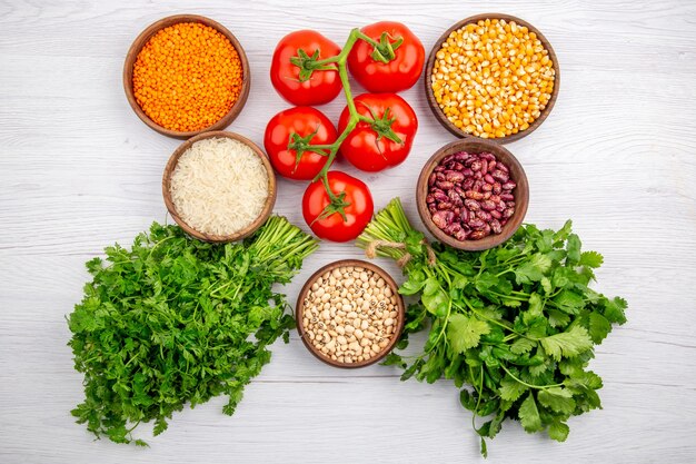 Vista superior de tomates frescos con tallo de maíz, lentejas amarillas, paquete de verduras, pimienta, arroz largo en mesa blanca