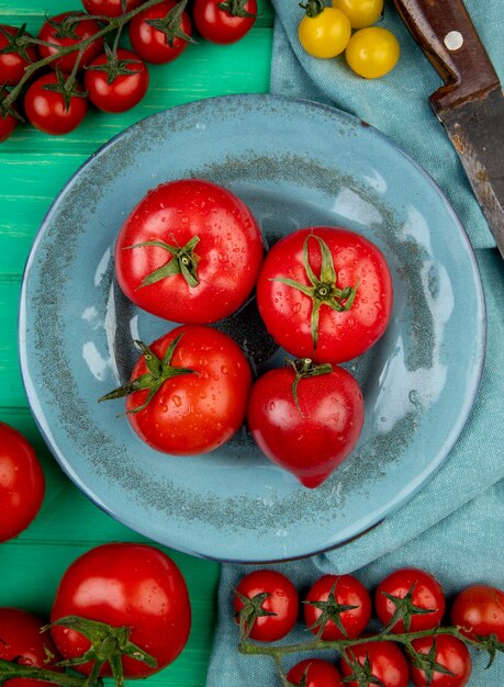 Vista superior de tomates en placa con otros y cuchillo en superficie verde