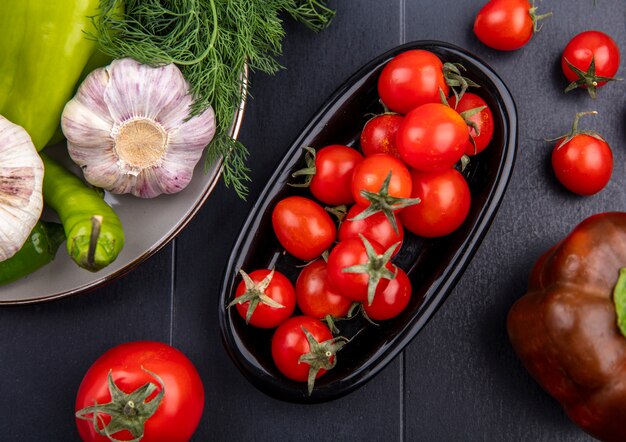 Vista superior de tomates en plato y plato de eneldo ajo pimiento sobre superficie negra