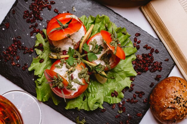 Vista superior de tomates rellenos con salsa sobre una hoja de lechuga con rodajas de limón y agracejo seco