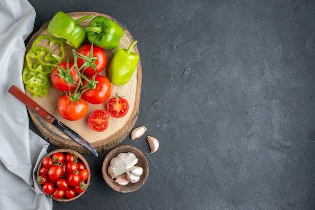 Vista superior de tomates rojos frescos con ajo y pimientos verdes sobre superficie oscura