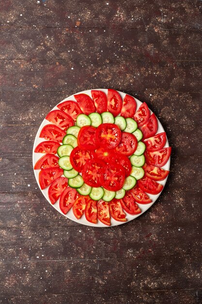 Vista superior de tomates rojos frescos en rodajas con ensalada fresca de pepinos en el espacio marrón