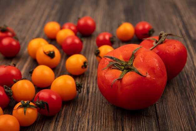 Vista superior de tomates rojos redondeados suaves con tomates cherry rojos y naranjas aislados en una superficie de madera