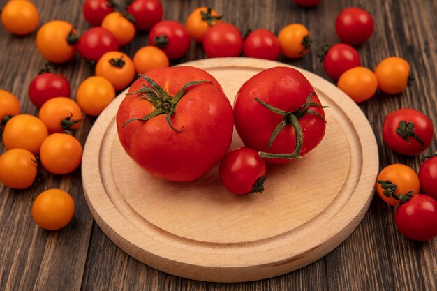 Vista superior de tomates rojos suaves en una tabla de cocina de madera con tomates cherry aislado en una pared de madera