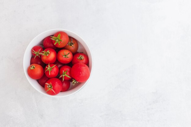 Vista superior de tomates rojos en el tazón de fuente blanco sobre fondo blanco