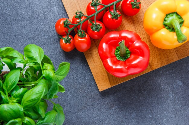 Vista superior de tomates en la tabla de cortar con pimientos, verdes en superficie gris. horizontal