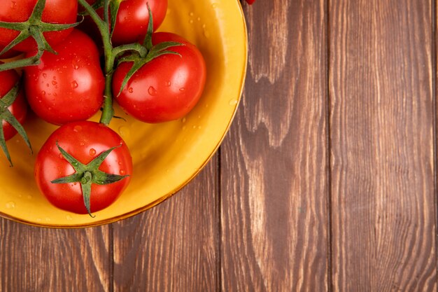 Vista superior de tomates en un tazón en el lado izquierdo y madera con espacio de copia