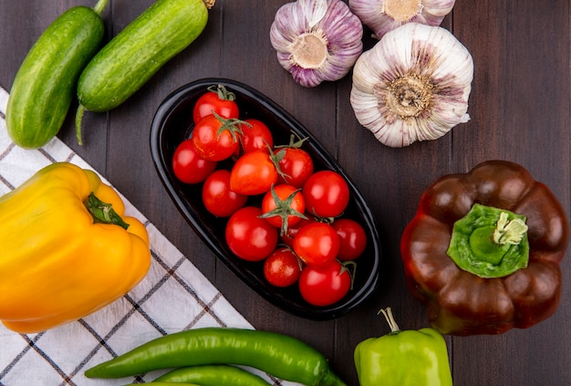 Vista superior de tomates en un tazón y pepino ajo pimienta alrededor sobre superficie de madera