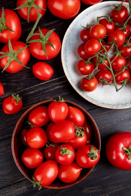 Vista superior de tomates en un tazón y plato y otros en madera