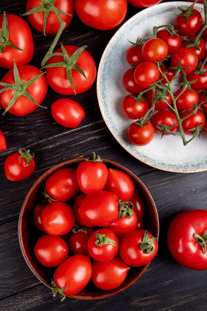 Vista superior de tomates en un tazón y plato y otros sobre superficie de madera