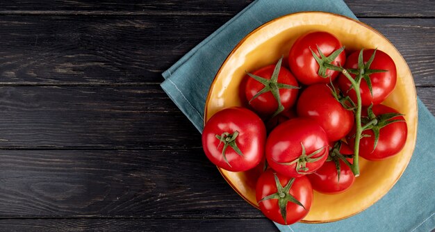 Vista superior de tomates en un tazón sobre tela azul y superficie de madera con espacio de copia