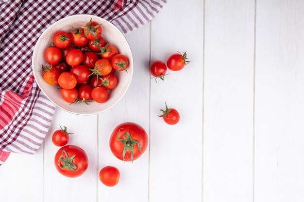 Vista superior de tomates en un tazón sobre tela escocesa y sobre superficie de madera