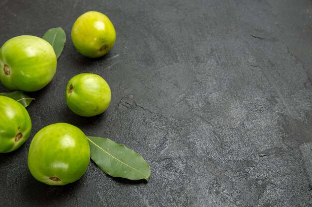 Vista superior de tomates verdes y hojas de laurel a la izquierda del suelo oscuro con espacio de copia