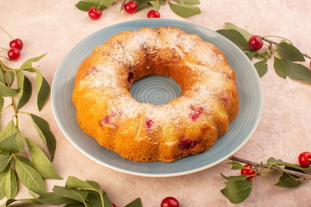 Una vista superior de la torta de cereza redonda formada dentro de la placa en el escritorio rosa pastel galleta azúcar dulce