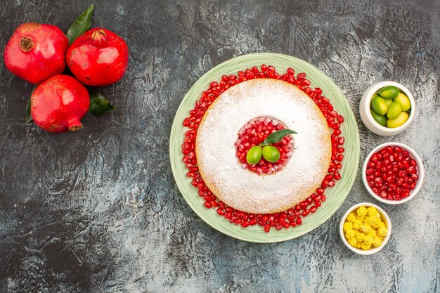 Vista superior de la torta y dulces tazones de un pastel de frutas cítricas dulces tres granadas rojas