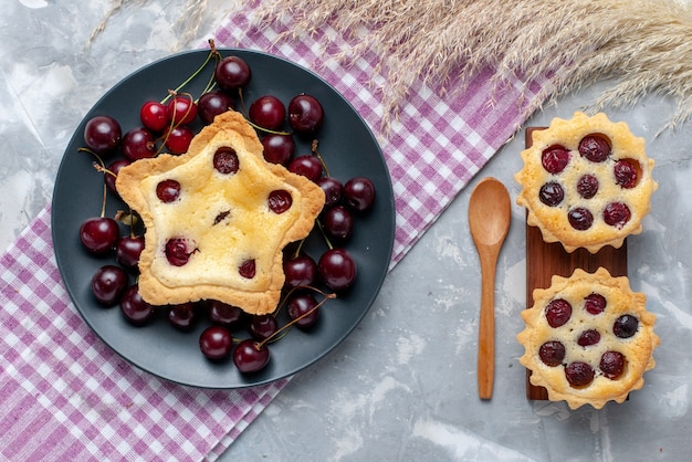 Vista superior de la torta en forma de estrella junto con tortas de cereza y guindas frescas en la mesa de luz pastel de frutas frescas hornear pastel