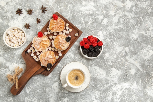 Vista superior de tortas dulces con caramelos y taza de café sobre fondo blanco.