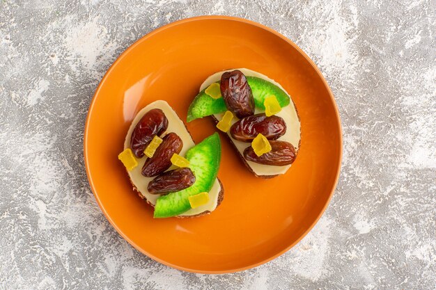 Vista superior de tostadas de pan con pepino y ciruelas secas dentro de la placa naranja en la pared blanca pan tostado sándwich comida desayuno