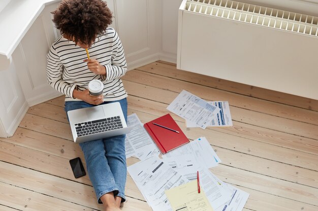 Vista superior del trabajador autónomo ocupado con corte de pelo afro, trabaja en un proyecto en línea