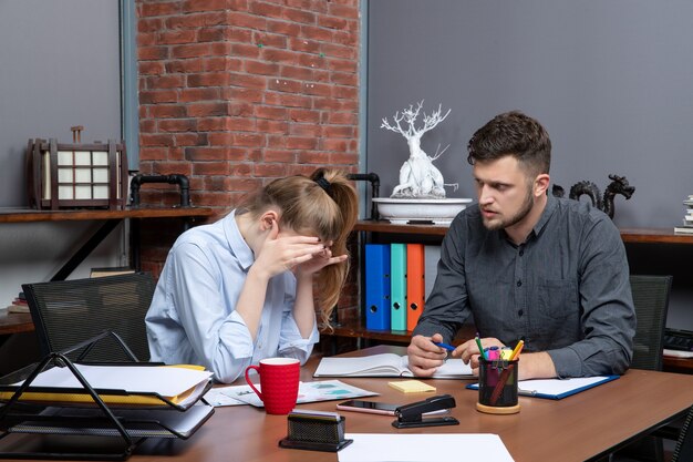 Vista superior de la trabajadora joven cansada y su compañero de trabajo masculino sentado en la mesa en el entorno de oficina