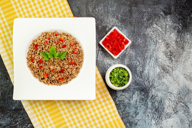 Foto gratuita vista superior del trigo sarraceno cocido sabroso dentro de la placa blanca con verduras en el color de la mesa gris claro