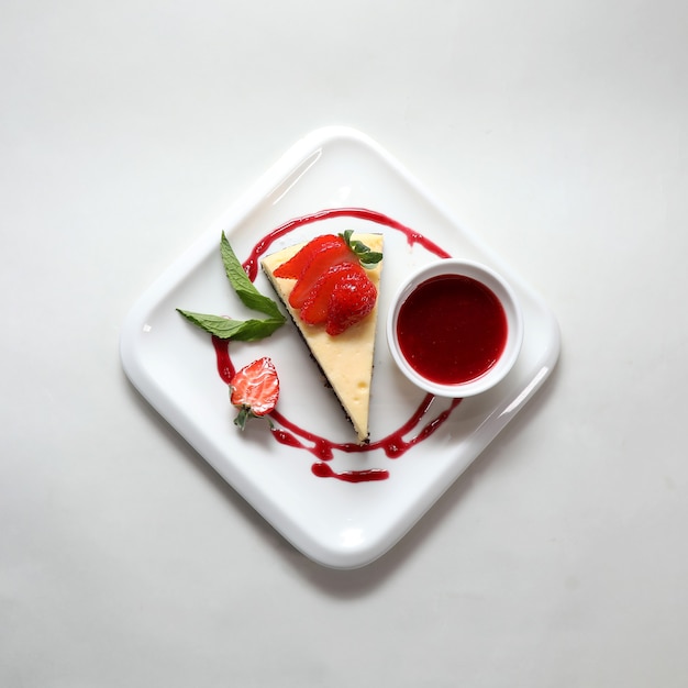 Vista superior de un trozo de tarta de queso con una fresa en un plato aislado sobre un fondo blanco.