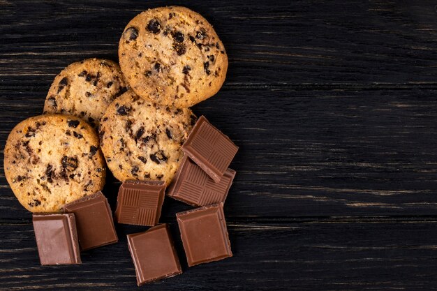 Vista superior de trozos de chocolate con leche y galletas de avena sobre fondo rústico oscuro