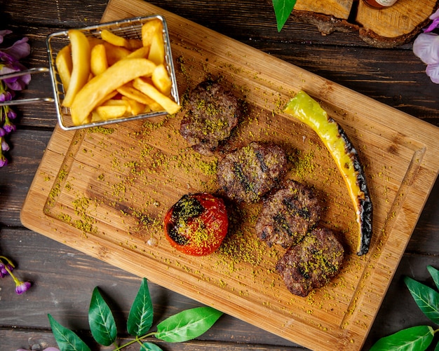 Vista superior de trozos de filete de cordero servido con papas fritas, pimiento asado y tomate