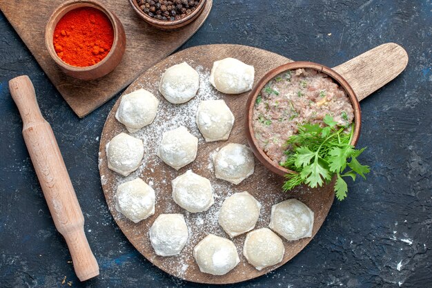 Vista superior de trozos de masa enharinada con verduras de carne picada junto con pimienta en la oscuridad, pasta de cena de carne cruda de alimentos de masa